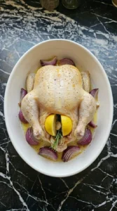Chicken roasting in a white ceramic dish with red onion wedges turning lightly golden