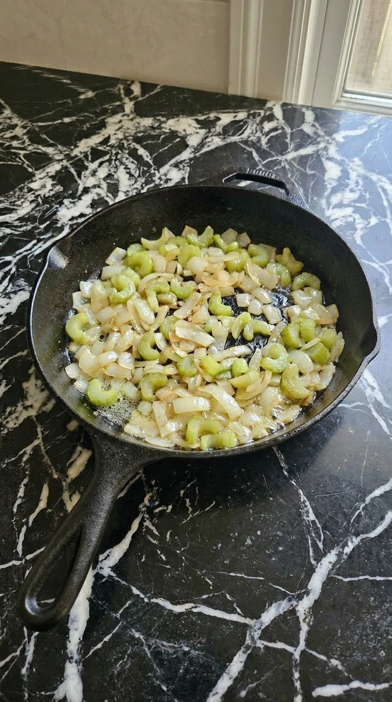 Sautéed onion and celery cooking in a cast-iron skillet