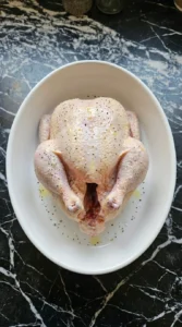 Seasoning a raw whole chicken with olive oil salt and pepper in a white roasting dish