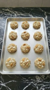 Twelve shaped banana pudding cookie dough portions on a baking tray