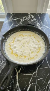 White garlic butter cream sauce simmering gently in a cast iron skillet