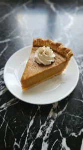 A single slice of pumpkin pie garnished with whipped cream on a plate