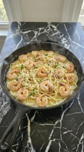 Tossing spaghetti and seared shrimp in garlic cream sauce inside a skillet