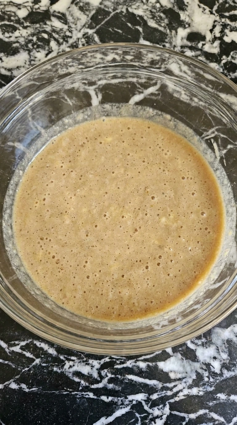Bubbly light brown liquid mixture of wet ingredients in a glass bowl