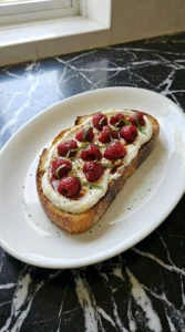 A single Raspberry Ricotta Toast topped with roasted berries, basil and honey balsamic syrup.