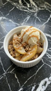 Served Caramel Pear Crisp with vanilla bean ice cream and warm caramel in a white ramekin.