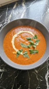 Served Creamy Roasted Red Pepper and Tomato Soup with an uneven cream swirl, basil and black pepper