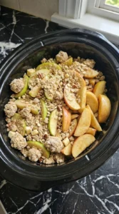 Crockpot Apple Crisp Recipe — Easy Slow Cooker Apple Crisp for Fall step three layered inside a slow cooker with apple wedges and oat crumble