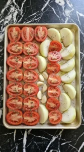 Halved Roma tomatoes and onion seasoned for Easy Sheet Pan Tomato Soup With Fresh Tomatoes.