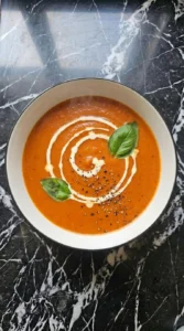 Easy Slow Cooker Tomato Soup for Cozy Fall Dinners served in a shallow white bowl with a loose cream swirl, torn basil and cracked black pepper