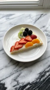 A plated wedge of Halloween Fruit Pizza with Sugar Cookie Crust showing its layers