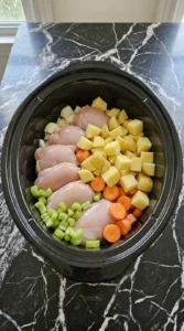 Healthy Soup Recipes for Crockpot Nights That Feel Cozy and Easy with raw chicken thighs layered beneath potatoes orange carrots celery and onion