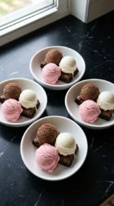 Layering brownies and three ice cream flavors for Neapolitan Ice Cream Sundae (Strawberry, Chocolate & Vanilla) in chilled white bowls.