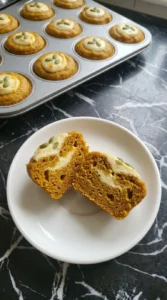 Split pumpkin cream cheese muffin showing moist crumb and a creamy white center.