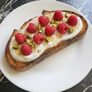 Raspberry Yogurt Toast topped with fresh berries and honey on a white plate