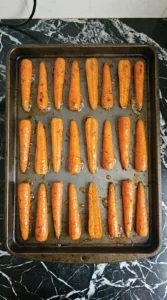 Maple glazed carrot halves roasting cut-side down on a sheet pan