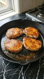 Four boneless pork chops with deep golden crusts after searing
