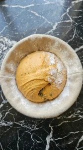 Shaped pumpkin sourdough boule cold-proofing in a round basket. Recipe focus: Fall Sourdough Recipes Bread.