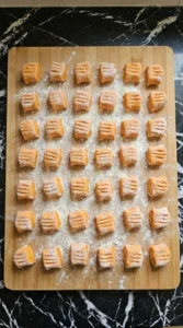 Thirty-six raw Sweet Potato Gnocchi pillows with shallow ridges and flour dusting.