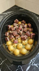 Layering potatoes and garlic butter sauce for Slow Cooker Garlic Butter Beef Bites and Potatoes