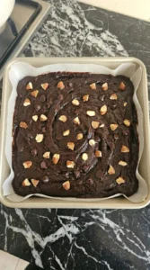 Sweet potato brownie batter topped with chocolate chips and almonds in a square pan.