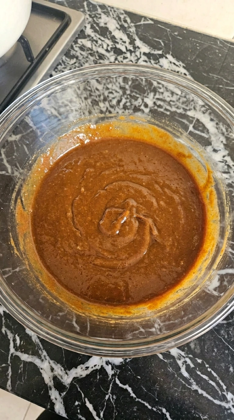 Glossy sweet potato brownie wet mixture in a clear glass bowl.