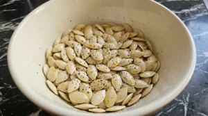 Roasted Pumpkin Seeds with Salt and Pepper step showing raw seeds coated with olive oil, salt and black pepper