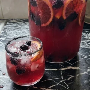 Big Batch Cocktails Halloween deep ruby punch with bubbles, black sugar rim, blackberries and blood orange. Recipe focus: easy big batch cocktails halloween.