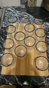 Big Batch Cocktails Halloween step showing 12 chilled glasses with uneven black sanding sugar rims. Recipe focus: easy big batch cocktails halloween.