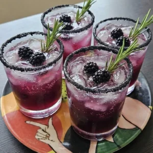 Halloween Cocktails in four rocks glasses with purple berry fizz, black sugar rims, blackberries and rosemary Recipe focus: easy halloween cocktails.