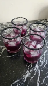 Halloween Cocktails step with four purple drinks over ice in rocks glasses with irregular black sanding sugar rims Recipe focus: easy halloween cocktails.