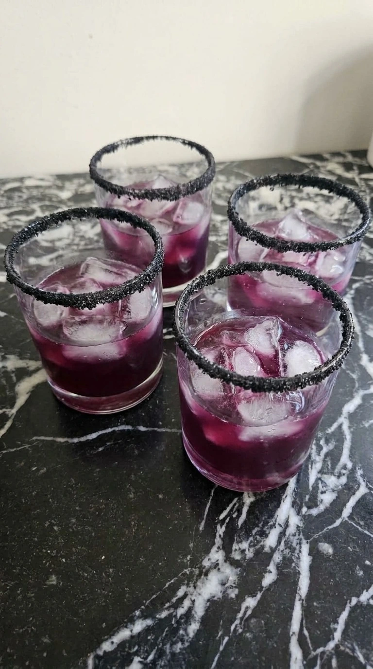 Halloween Cocktails step with four purple drinks over ice in rocks glasses with irregular black sanding sugar rims Recipe focus: easy halloween cocktails.