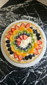 Halloween Fruit Pizza frosted and topped with uneven arcs of strawberries, kiwi, citrus and dark berries Recipe focus: halloween finger foods appetizers.