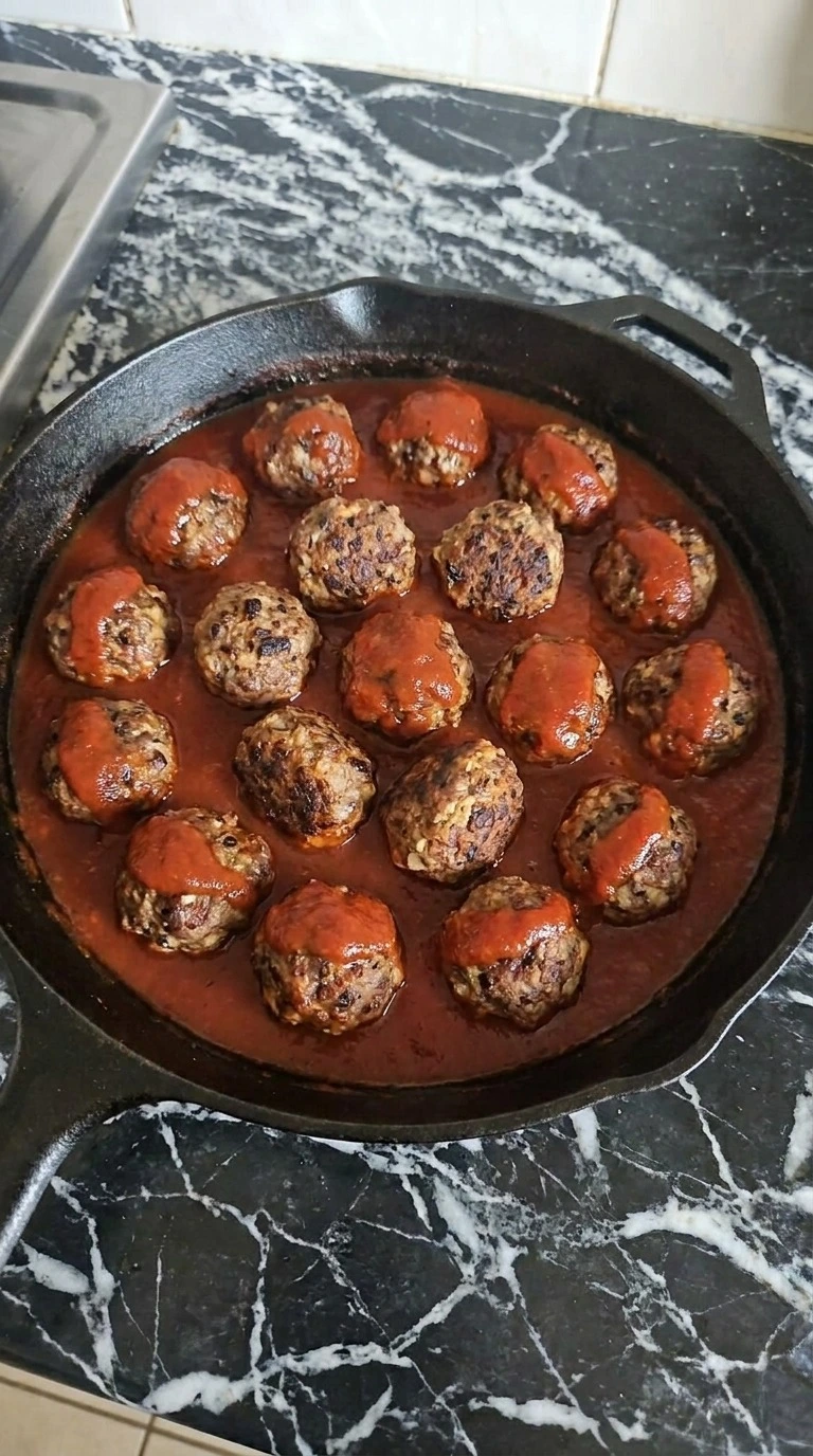 Halloween Party Food Meatballs simmering in glossy tomato basil marinara with browned edges visible