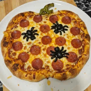 Halloween Party Food Pizza with golden crust, bubbling cheese, pepperoni, olive spiders and a green pepper stem