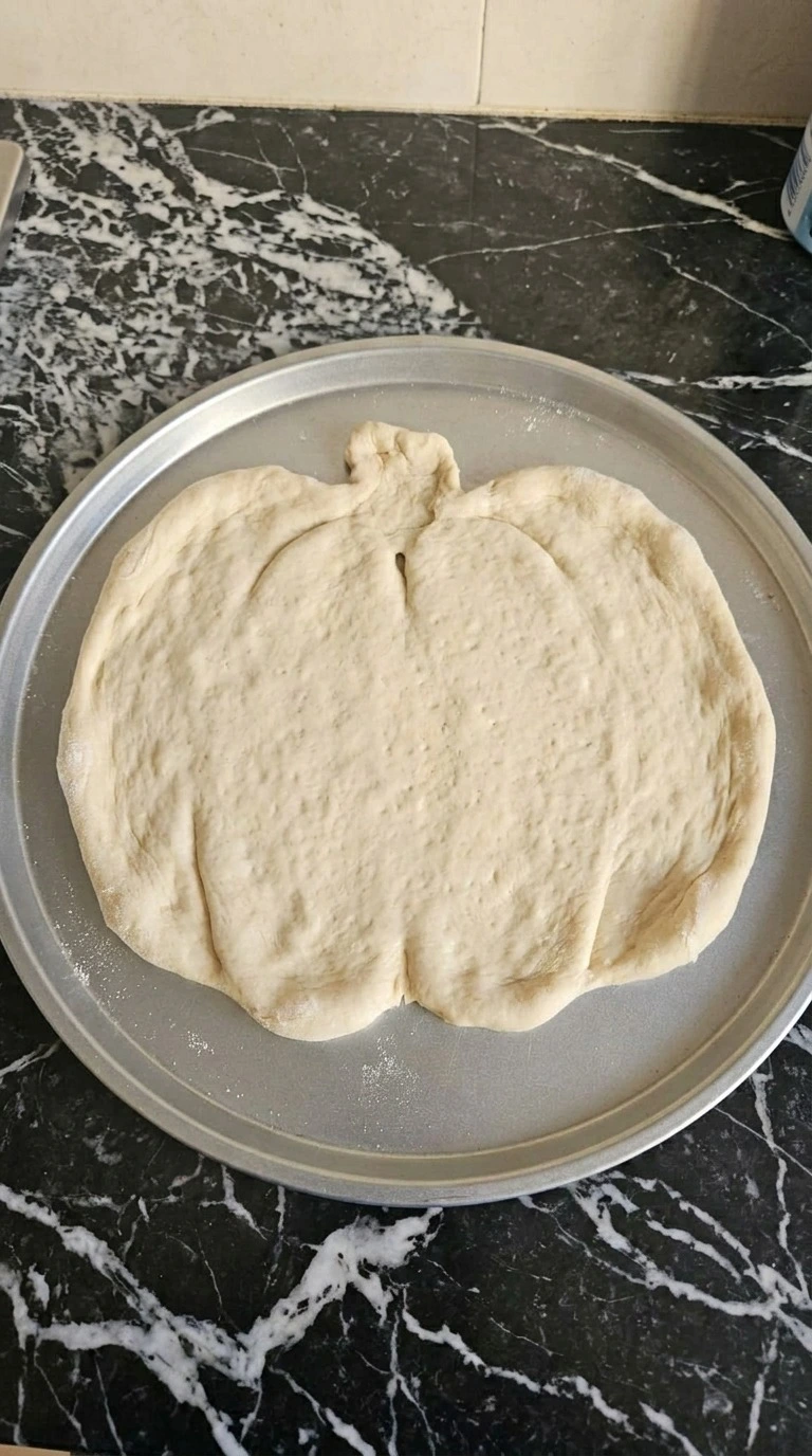 Halloween Party Food Pizza dough shaped into an uneven 12-inch pumpkin round before topping