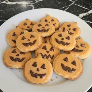 Halloween Pumpkin Designs shown as orange glazed pumpkin sugar cookies with chocolate jack-o'-lantern faces