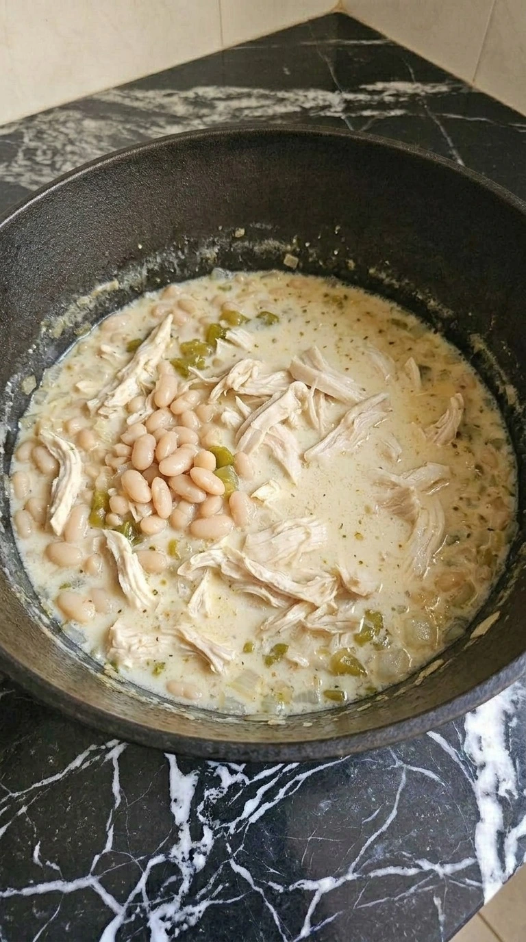 Creamy White Chicken Chili turning thick and ivory-colored as cream cheese melts around chicken and beans Recipe focus: easy white chicken chili.