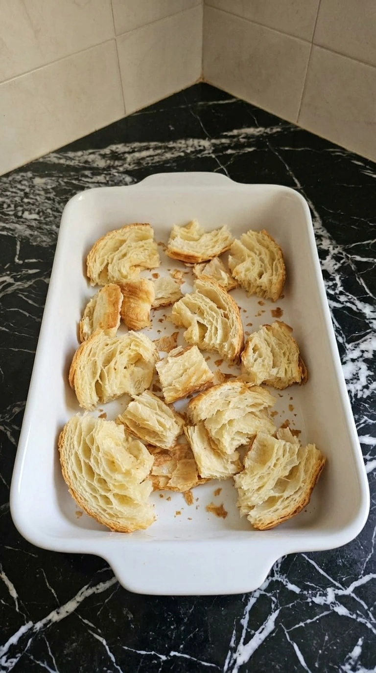 Croissant Breakfast Casserole step 1 with torn croissant pieces in baking dish Recipe focus: overnight breakfast casserole.
