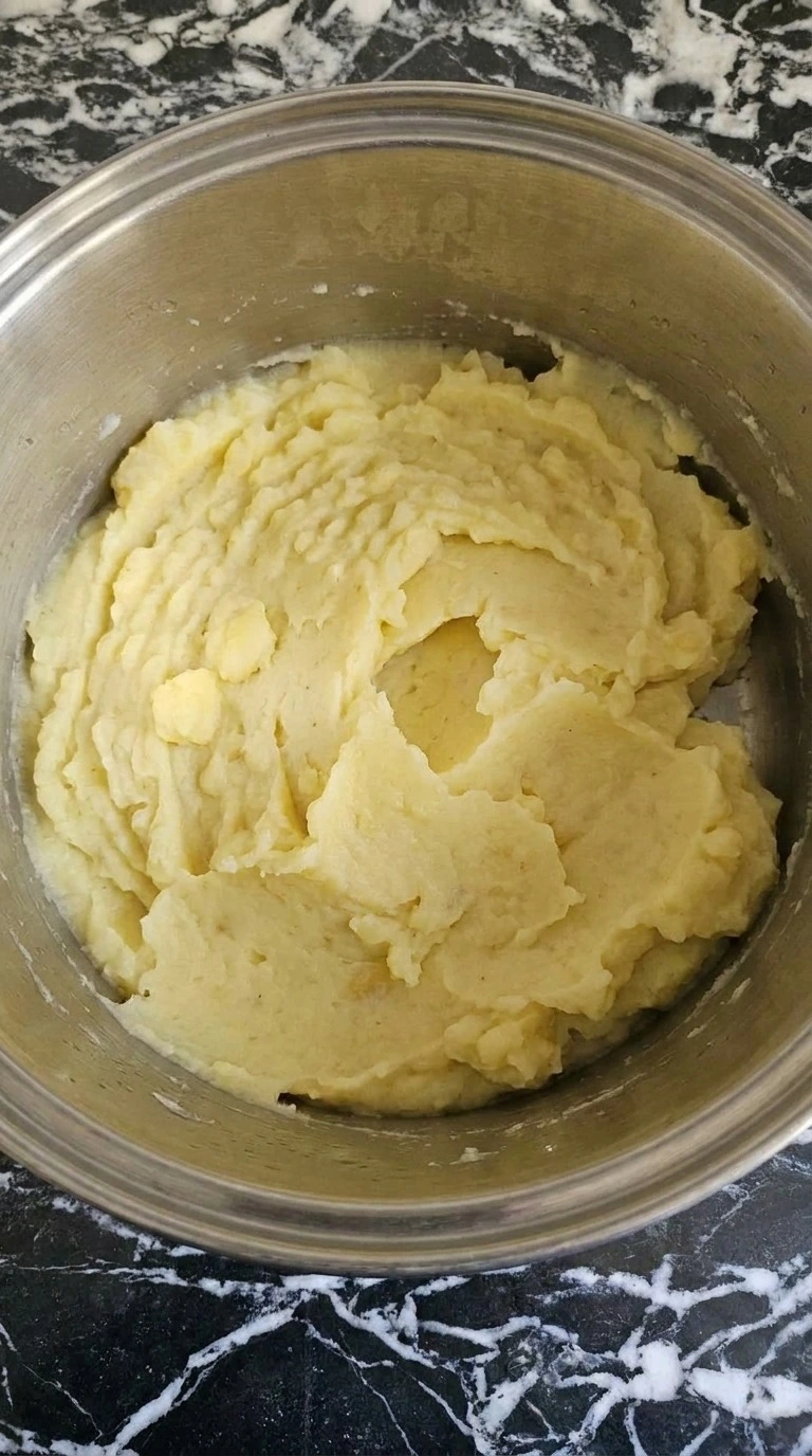 Make Ahead Mashed Potatoes being mashed into thick pale yellow fluffy potato folds Recipe focus: thanksgiving make ahead mashed potatoes.